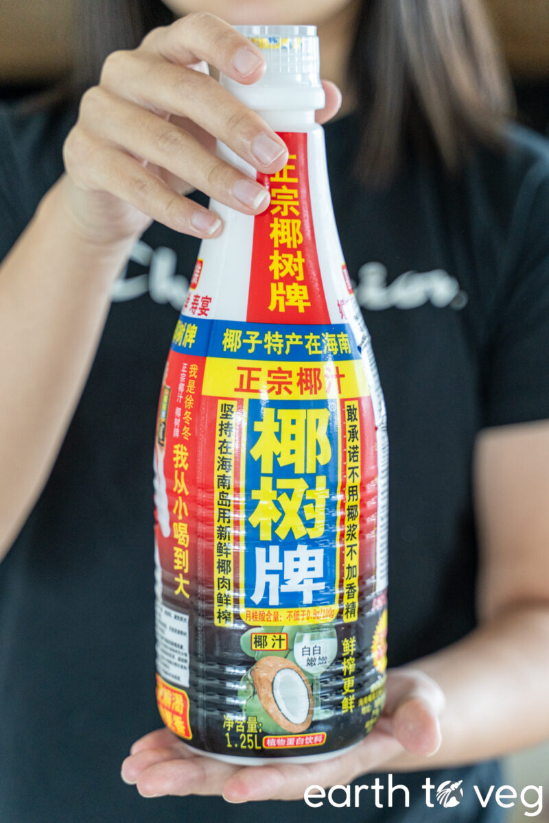 A girl holds up a bottle of Yeshu Hainan Coconut Drink beverage.