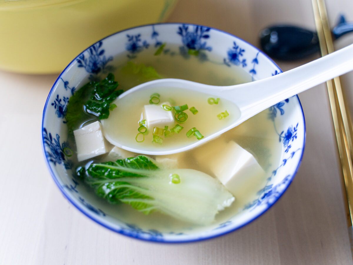 A small soup spoon rests in a blue porcelain bowl full of bok choy miso soup.