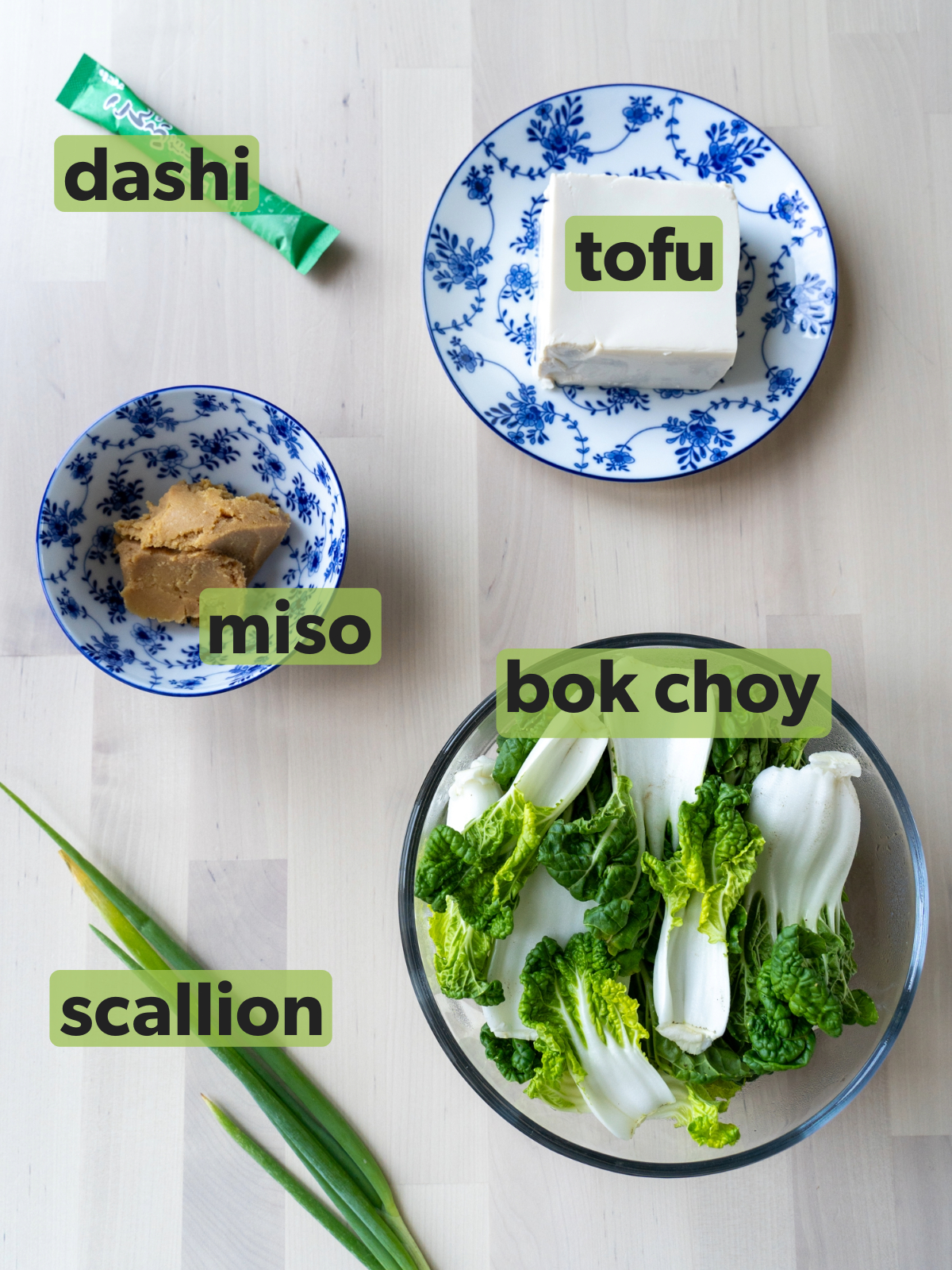 Ingredients for bok choy miso soup are laid out on a wooden table.