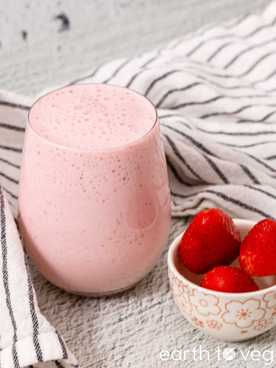 Strawberry coconut smoothie in a glass beside fresh strawberries and a striped towel.